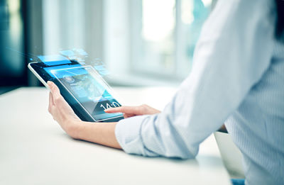 Picture of a female sitting at a table, looking at news on an Ipad.